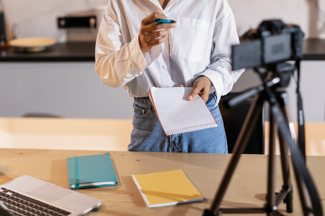 About Vlogger recording content with a camera, holding notes and using a laptop in a modern setting.